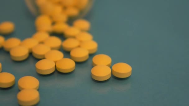 Zeitlupe: Ein Glas fällt, aus dem gelbe Tabletten auf einen blauen Glastisch fallen — Stockvideo