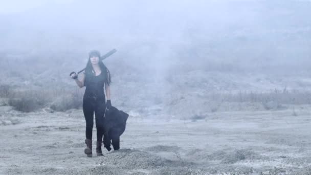流氓团伙的残忍女人拿着棒球棒走着，把烟撒在荒原上 — 图库视频影像