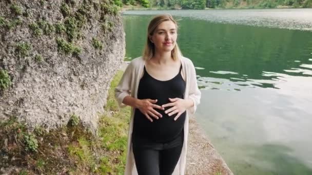 Zwangere vrouw wandelen in de buurt van het meer in de zomer bos. — Stockvideo