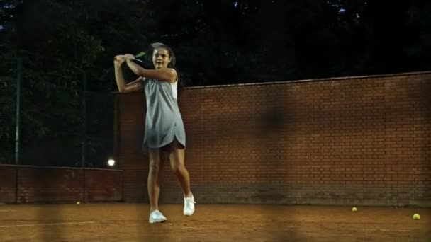 Spelar tennis på natten. ung flicka blockerar bollen med tennisracket under träningen — Stockvideo