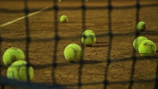 Tennis balls lie on the tennis court. Blurred grid on the foreground. — Stock Video