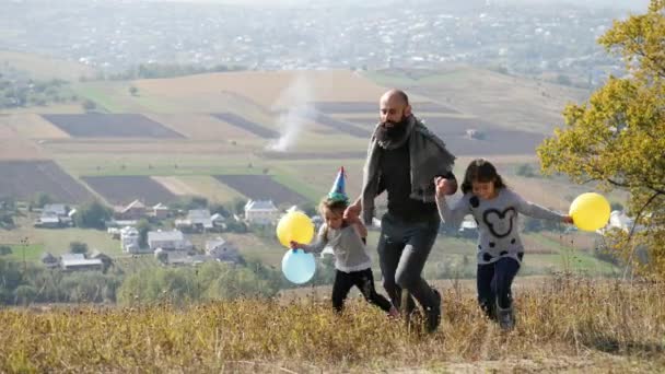 Батько з двома доньками з повітряними кулями, що біжать на лузі — стокове відео