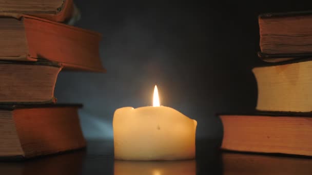 Pile di libri sono in piedi vicino a una candela accesa e fumo magico colorato sta volando . — Video Stock