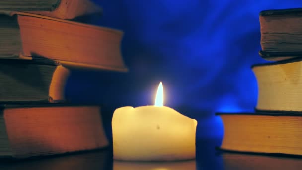 Piles of books are standing near a burning candle and colored magic smoke is flying. — Stock Video