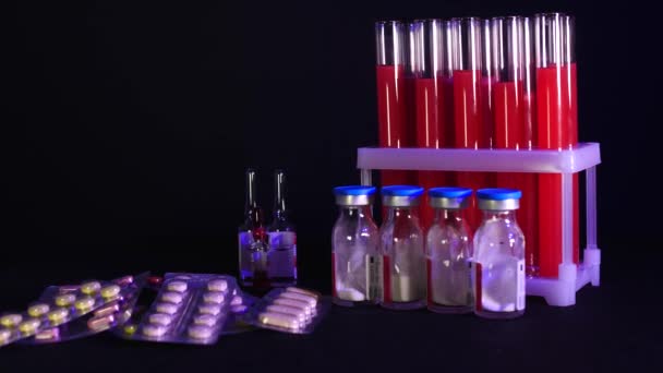 Pillen op een achtergrond van reageerbuisjes met rode vloeistof en ampullen op een zwarte achtergrond — Stockvideo
