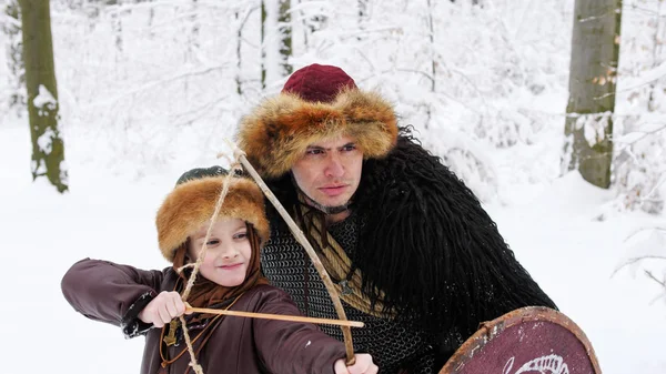 父バイキングは冬の森でアーチェリーに彼の息子を教える. — ストック写真