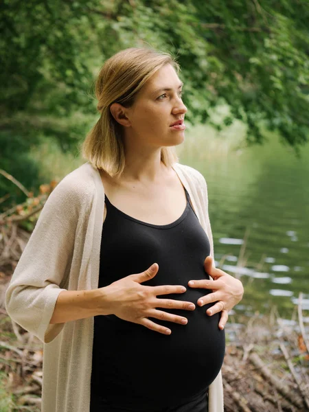 Gravid kvinna promenader nära sjön på sommaren skog. — Stockfoto