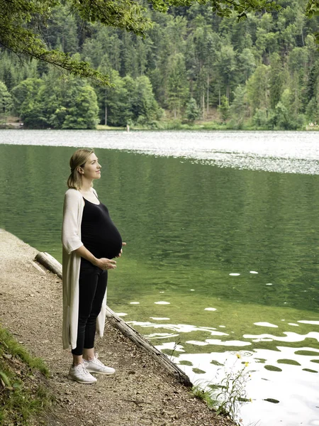 Vacker gravid kvinna nära en fjällsjö i skogen. — Stockfoto