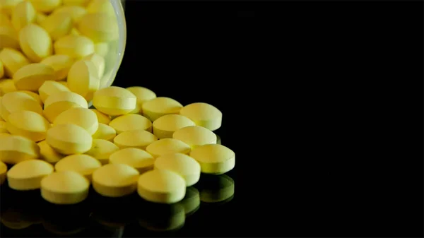 Yellow pills scattered from a transparent bottle are scattered on a glass black table — Stock Photo, Image