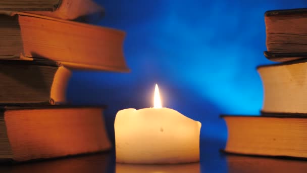 Kupa książek stoi przy płonącej świecy i latający kolorowy magiczny dym.. — Wideo stockowe