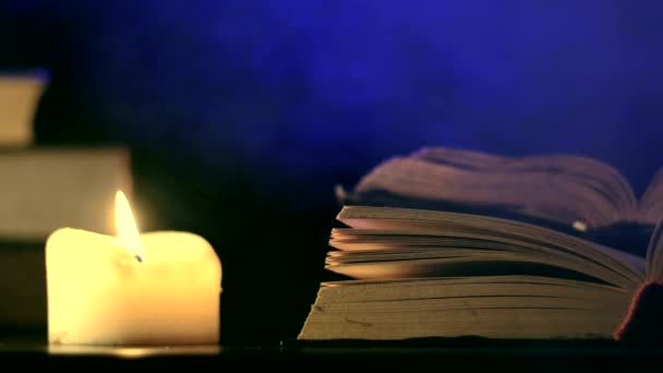 Κοντά στο ανοιχτό βιβλίο, ένα κερί καίει και χρωματιστές, μαγικές μύγες καπνού. — Αρχείο Βίντεο