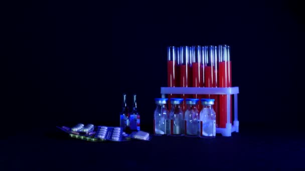 Pills on a background of test tubes with red liquid and ampoules on a black background — Stock Video