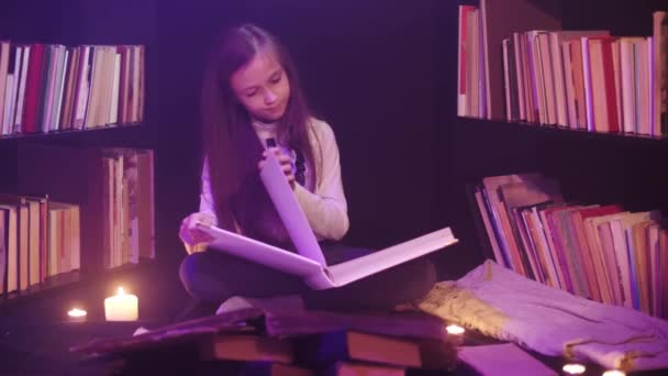 Дівчина відкриває казкову книгу в бібліотеці, кольорові димові круги навколо, свічки освітлені поруч — стокове відео