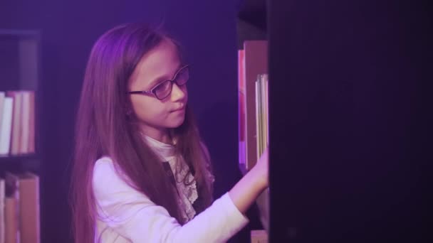 Una ragazza sta selezionando attraverso i libri sugli scaffali della biblioteca, il fumo magico sta girando intorno. — Video Stock