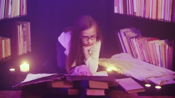 Une fille ouvre un livre de contes de fées dans la bibliothèque, de la fumée colorée tourbillonne, des bougies sont allumées à proximité — Video