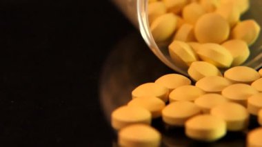 Yavaş Çekim: Cam bir kavanoz düşer ve sarı tabletler siyah cam bir masaya düşer.