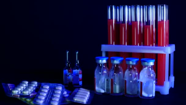 Pilules sur fond de éprouvettes avec liquide rouge et ampoules sur fond noir — Video