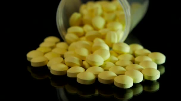 Gelbe Pillen aus einer durchsichtigen Flasche liegen auf einem schwarzen Glastisch verstreut — Stockvideo