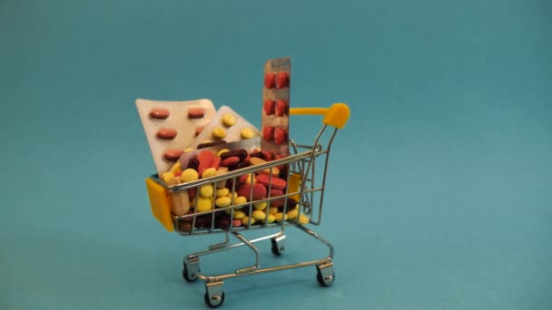 Тележка из супермаркета, заполненная медицинскими капсулами на синем фоне — стоковое видео