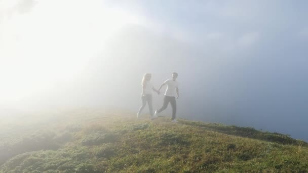 Jeune couple marchant sur une prairie de montagne sur fond de brouillard et de soleil . — Video