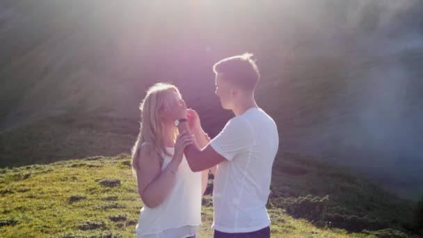 Pareja joven enamorada en un prado de montaña en el fondo de niebla y sol. — Vídeos de Stock