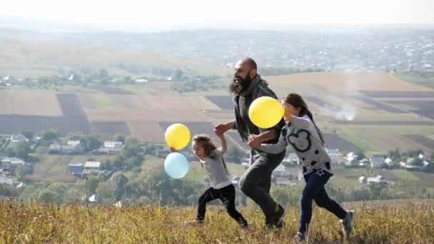 Padre con sus dos hijas con globos de aire corriendo en el prado — Vídeo de stock