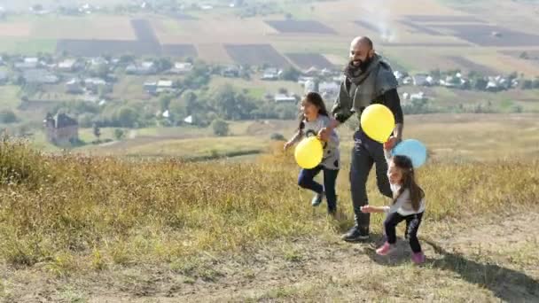 Padre con sus dos hijas con globos de aire corriendo en el prado — Vídeo de stock