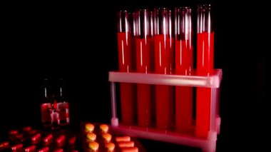 Siyah arka planda kırmızı sıvı bulunan test tüplerinin üzerindeki haplar.