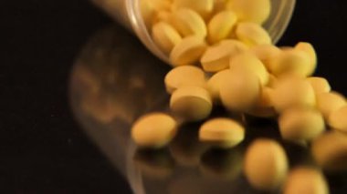 Yavaş Çekim: Cam bir kavanoz düşer ve sarı tabletler siyah cam bir masaya düşer.