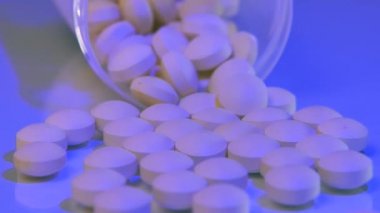 Pembe tabletler şeffaf bir şişeden düşüp mavi cam masaya saçılmış..