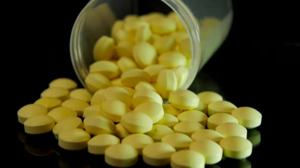 Желтые таблетки, разбросанные по прозрачной бутылке, разбросаны по стеклянному черному столу — стоковое видео