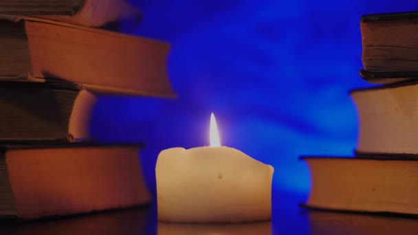 Pilhas de livros estão de pé perto de uma vela acesa e fumaça mágica colorida está voando . — Vídeo de Stock