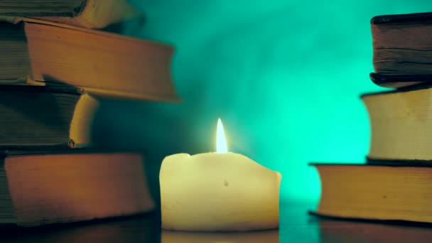 Hromádky knih stojí u hořící svíčky a barevný kouzelný kouř létá. — Stock video