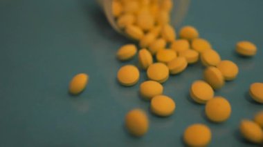 Yavaş Çekim: Cam bir kavanoz düşer ve sarı tabletler mavi cam bir masaya düşer.