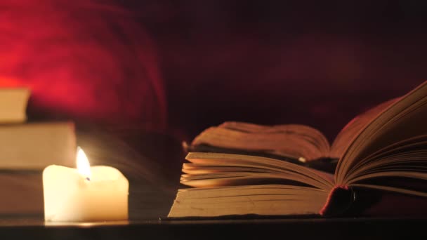 Pile di libri sono in piedi vicino a una candela accesa e fumo magico colorato sta volando . — Video Stock