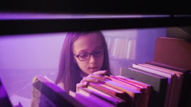 Uma menina está classificando através de livros nas prateleiras da biblioteca, fumaça mágica está girando ao redor. — Vídeo de Stock