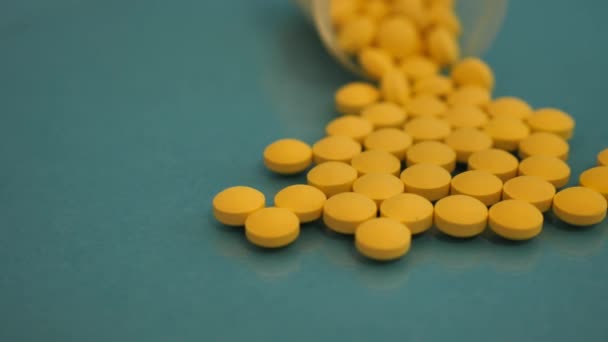 Pillole gialle sparsi su una bottiglia trasparente sono sparsi su un tavolo di vetro blu . — Video Stock