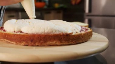 Sünger kekine krema sürmeye yakın çekim. Dönen bir stantta pasta.