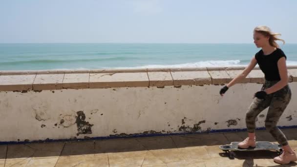 一个漂亮的金发姑娘在海滨的夏天热天坐在滑板上 — 图库视频影像