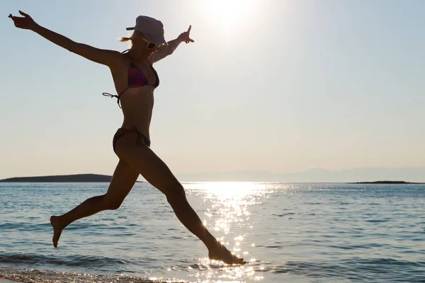 Wanita melompat cahaya latar di pantai — Stok Foto