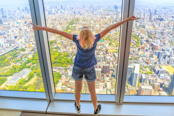 Aerial view of Osaka skyline in Japan. Travel and tourism asia concept. Young caucasian tourist woman with open arms enjoying Osaka cityscape from the observation deck.