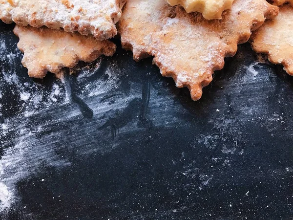 Festive cookies on a black kitchen board with powdered sugar
