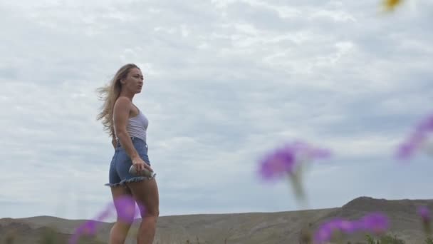 Kamera kövesse hipster fiatal nő fehér póló rövid farmer lengő hosszú haj. Egy lány táncol a hordozható zenei hangszóró okostelefon.