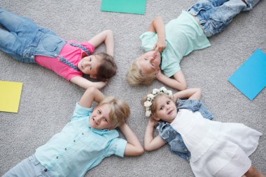 Dört mutlu çocuk yerde yatıyor ve renkli kağıtların arasında gülümsüyor.