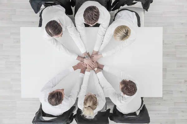 Business people team stacking hands sitting around white conference table in office unity cooperation concept