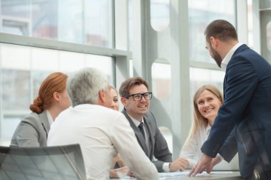 İş ekibi masanın başında oturuyor ve bürodaki belgelerle gülümsüyor.