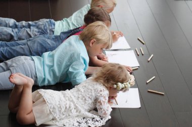 Cute little children friends drawing with pencils at home laying on floor clipart