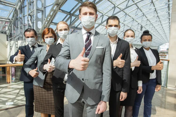Successful business people with thumbs up wearing surgical masks and standing together, healthcare and covid-19 prevention concept
