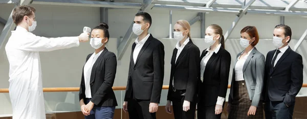 赤外線額温度計 温度計ガン を使用して保護外科用マスクを着用し 業務チームのウイルス症状の体温を確認します — ストック写真