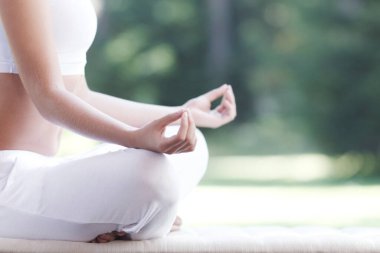 Beyaz spor kıyafetli genç bir kadın dışarıda yoga lotusu egzersizi yapıyor.